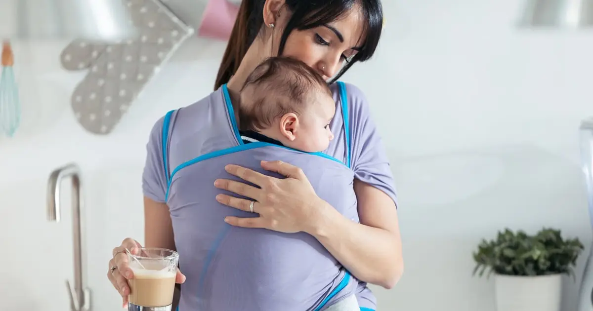 Mother holding baby in front-facing baby carrier at home